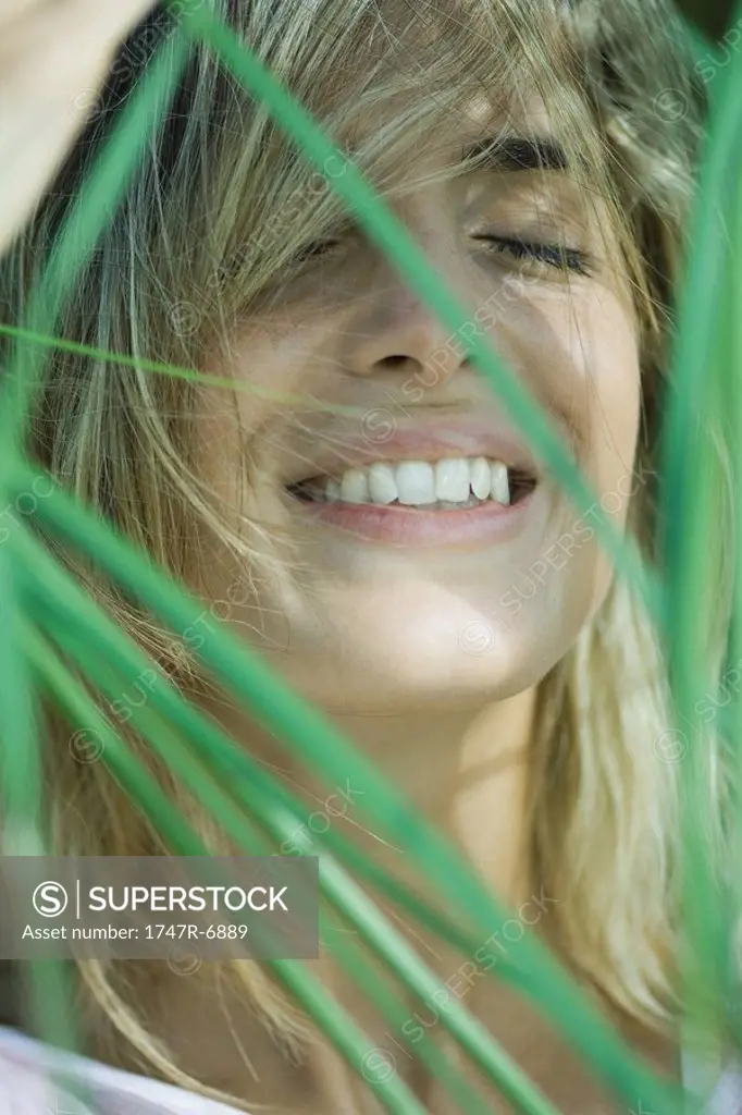Young woman among foliage, hair in face, smiling, eyes closed