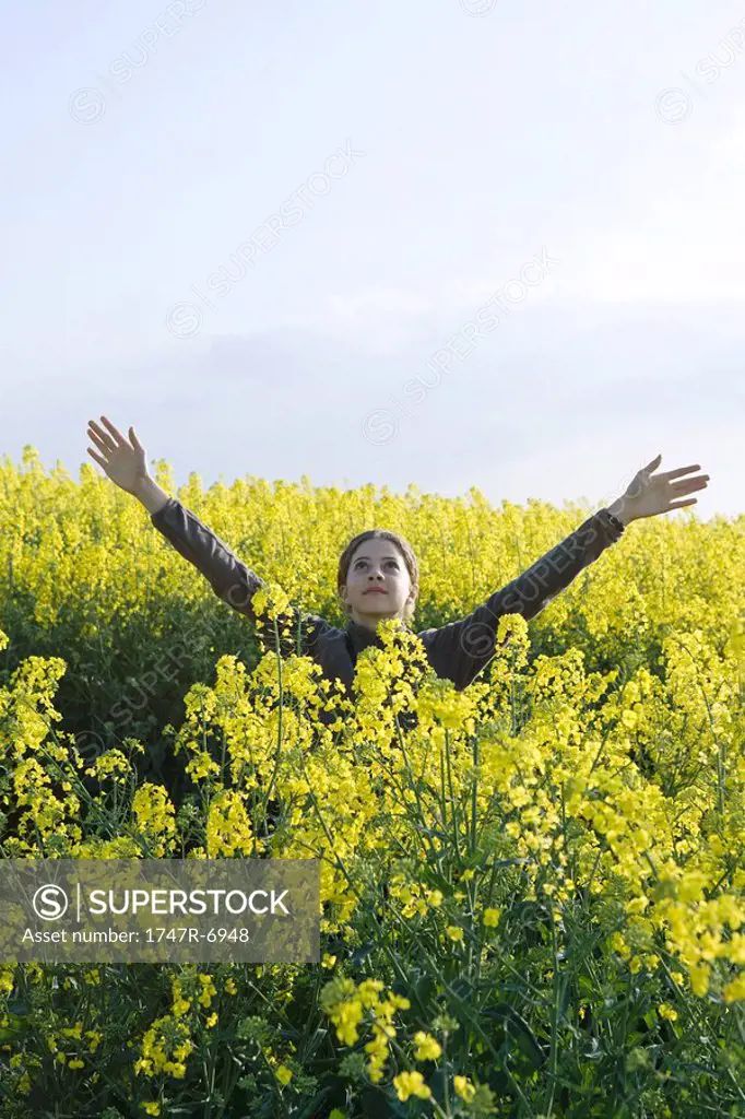Teen girl standing in field of canola in bloom