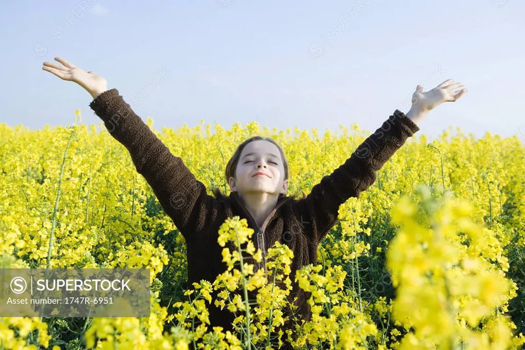 Girl standing in field of canola in bloom, head back, eyes closed and arms raised