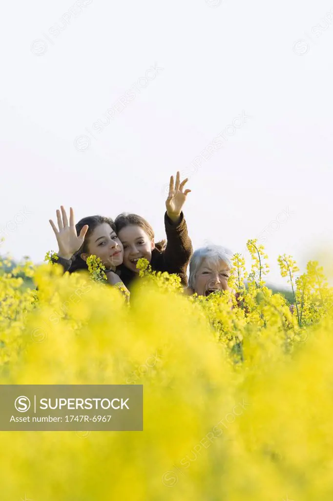 Senior woman and two granddaughters standing in field, waving at camera