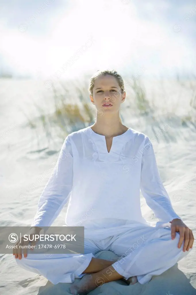Young woman sitting on dunes, full length