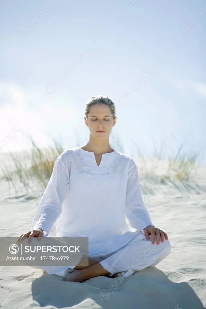 Young woman sitting on dune, eyes closed
