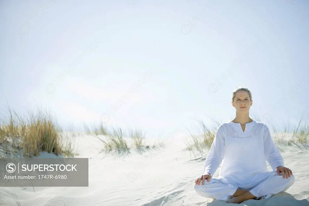 Young woman sitting on dune, full length