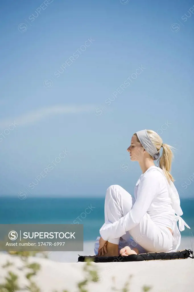Young woman sitting on beach with knee up, eyes closed