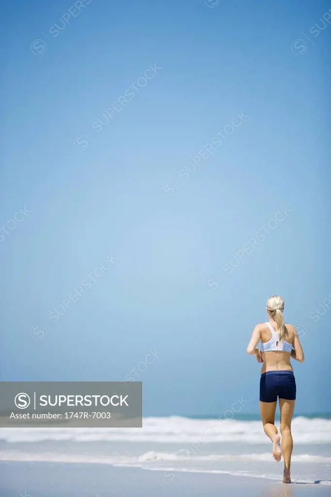 Young woman jogging on beach, rear view, full length
