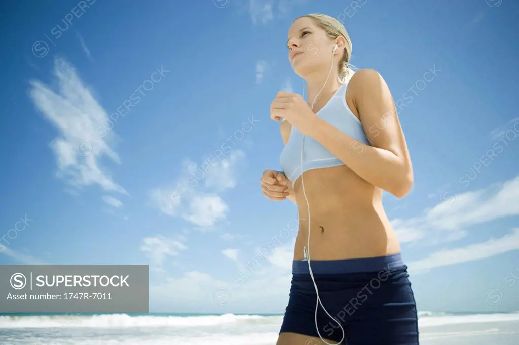Young woman jogging on beach, listening to MP3 player, low angle view