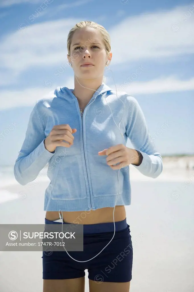 Young woman jogging on beach, listening to MP3 player