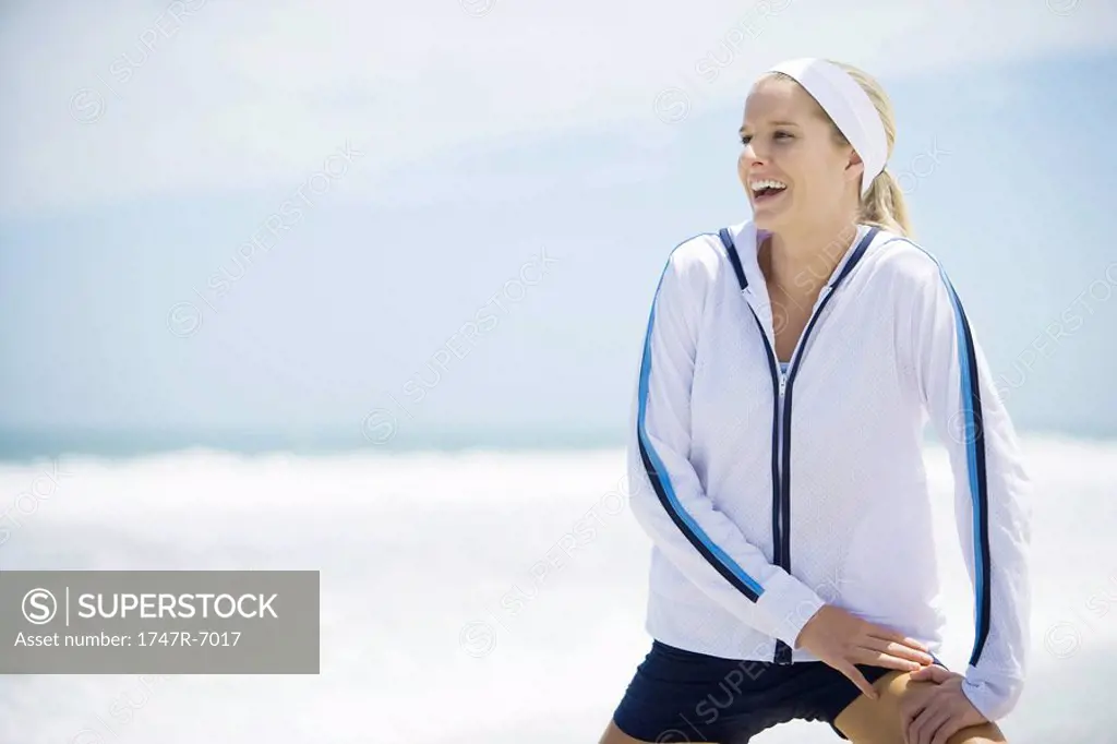 Young woman in active wear on beach, stretching and laughing