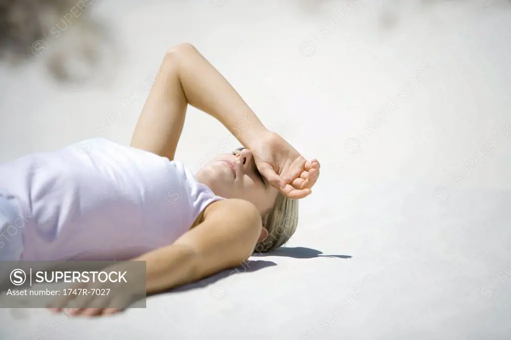 Young woman lying on beach, covering eyes with hand