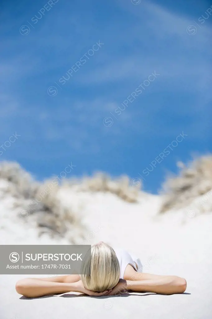 Young woman lying on beach, hands behind head