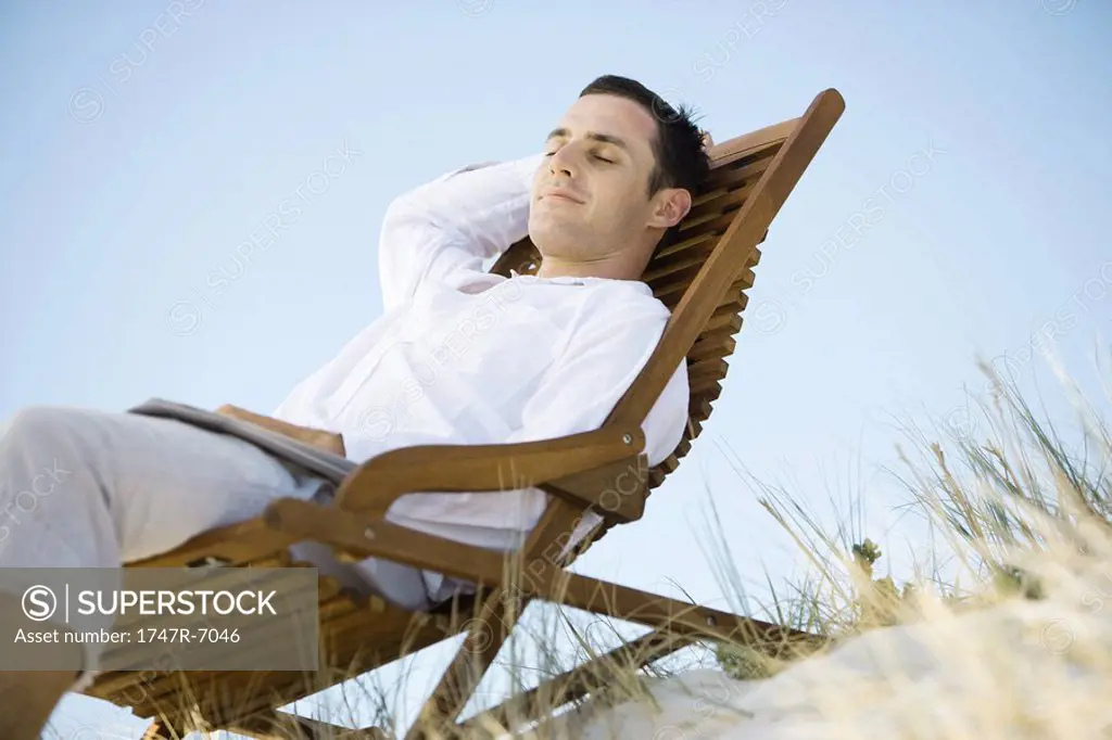 Young man sitting in deck chair, smiling, low angle view