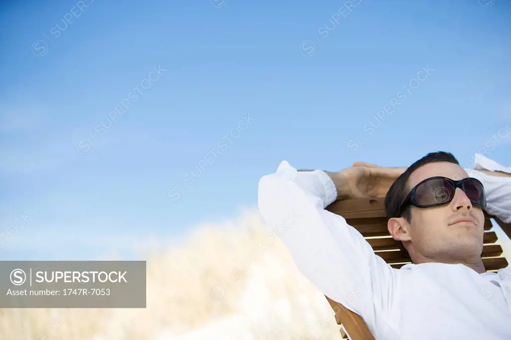 Young man sitting in deck chair, wearing sunglasses