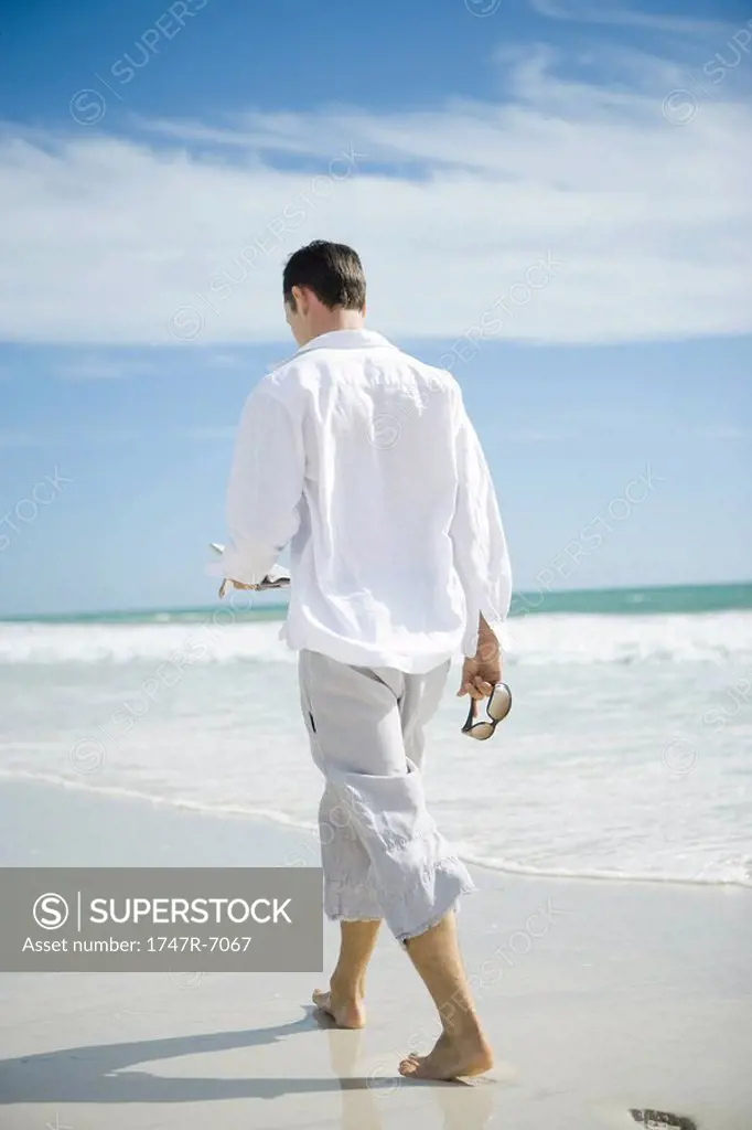 Young man walking on beach, rear view