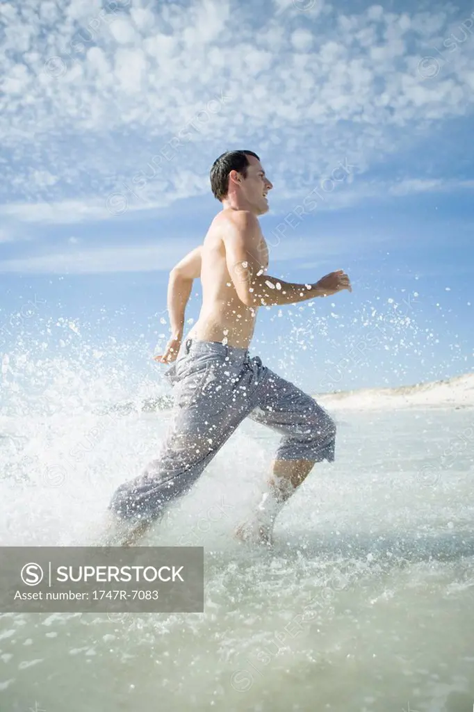 Young man running through surf on beach, full length, side view