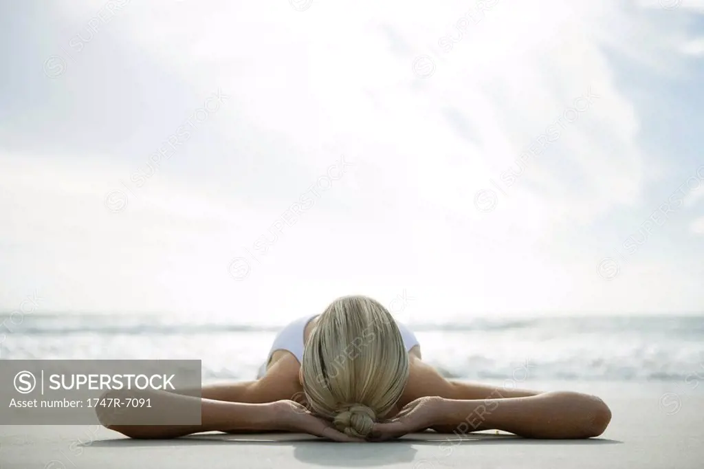 Young woman lying on back on beach with hands behind head, surface level view