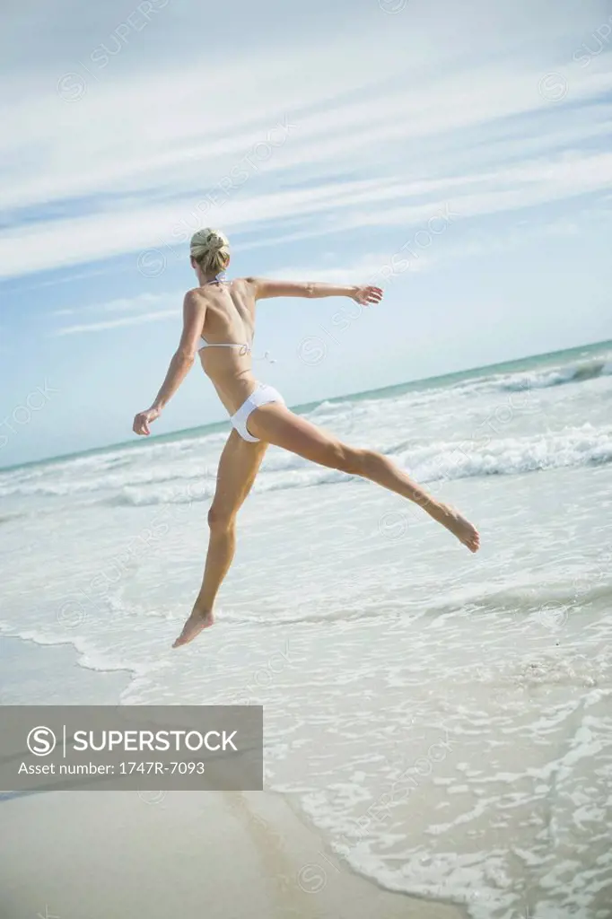 Young woman in bikini, leaping in surf, in mid air