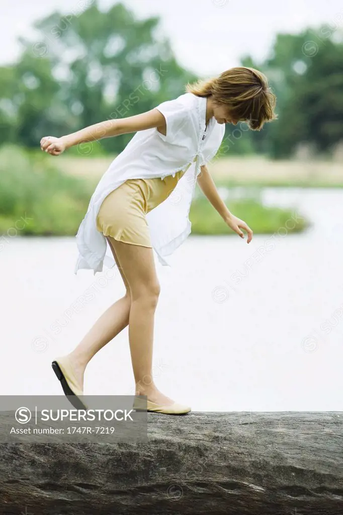 Young woman walking across log with arms out, looking down
