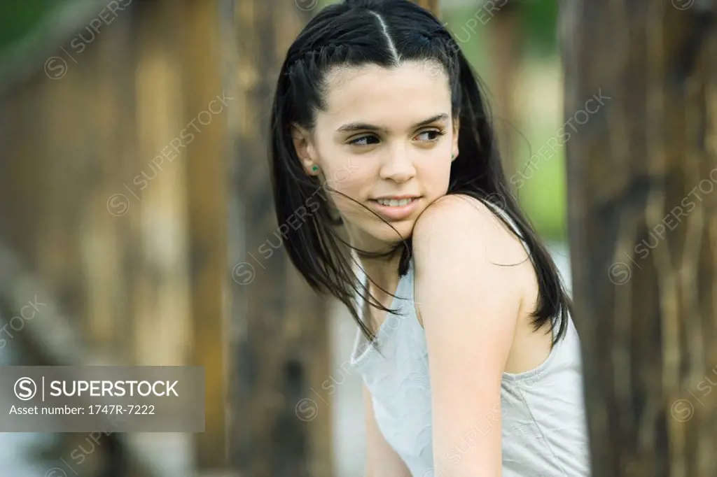 Teenage girl sitting outdoors, looking over shoulder, smiling