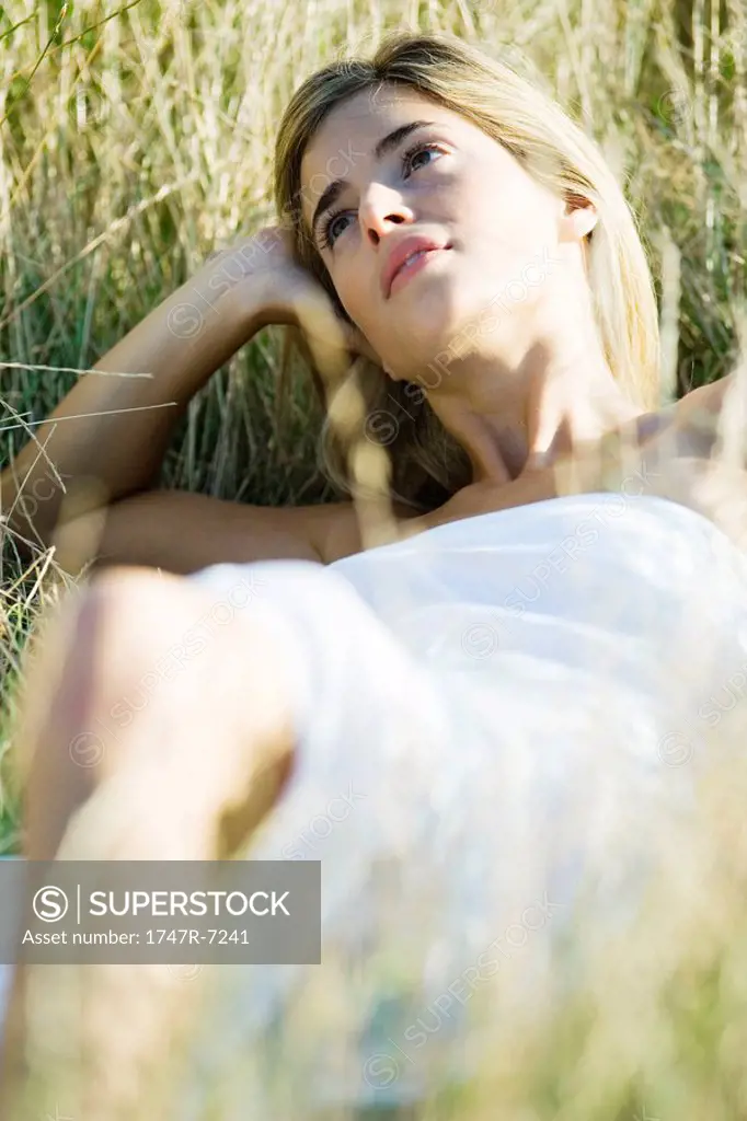 Young woman reclining in tall grass, holding head and looking away