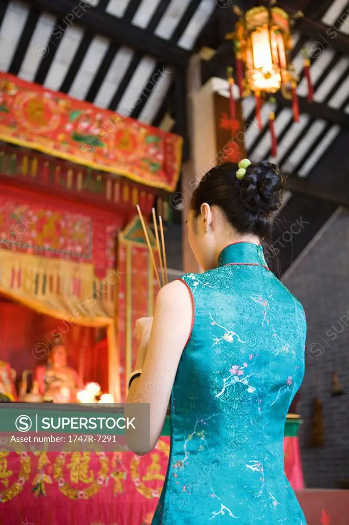 Young woman wearing traditional Chinese clothing, holding incense in temple