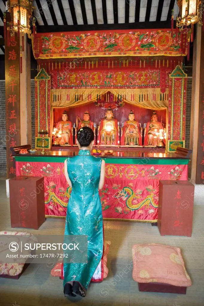 Young woman wearing traditional Chinese clothing, kneeling in front of shrine