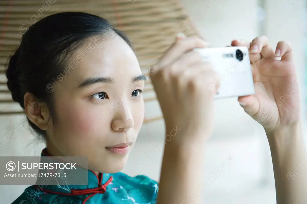 Young woman wearing traditional Chinese clothing, taking photo with digital camera