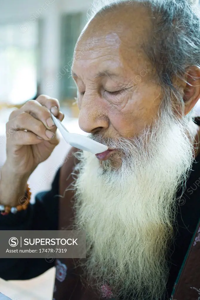 Elderly man wearing traditional Chinese clothing, eating with soup spoon