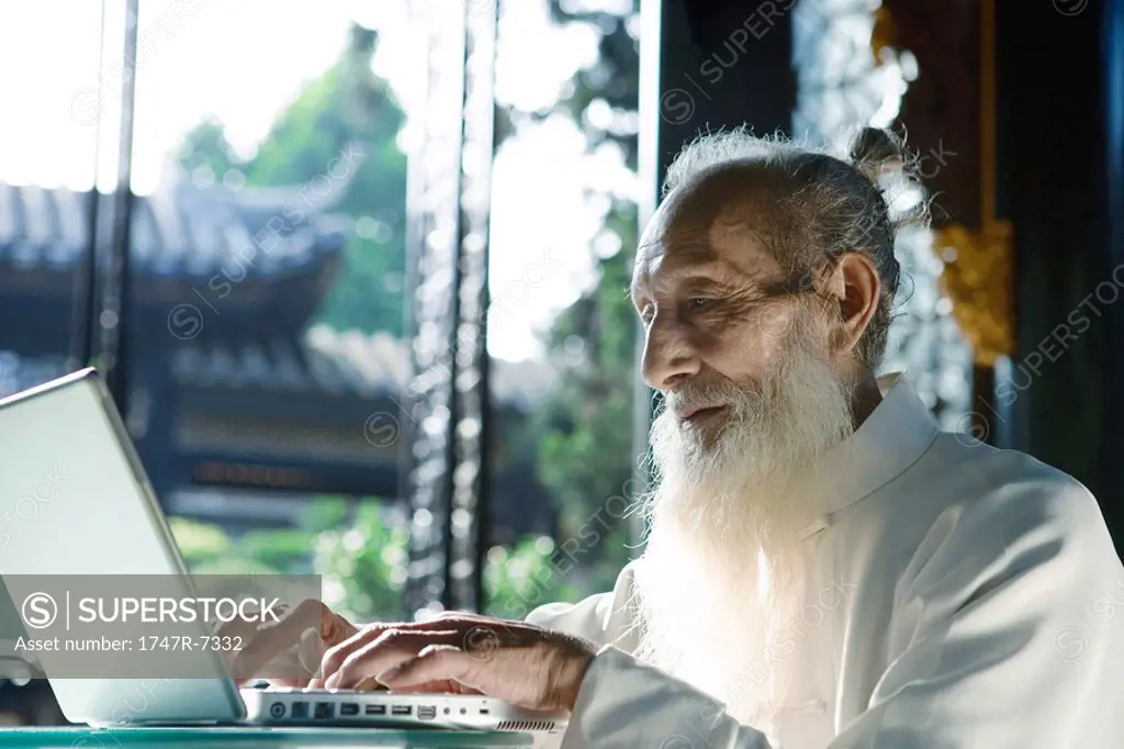 Elderly man wearing traditional Chinese clothing, using laptop