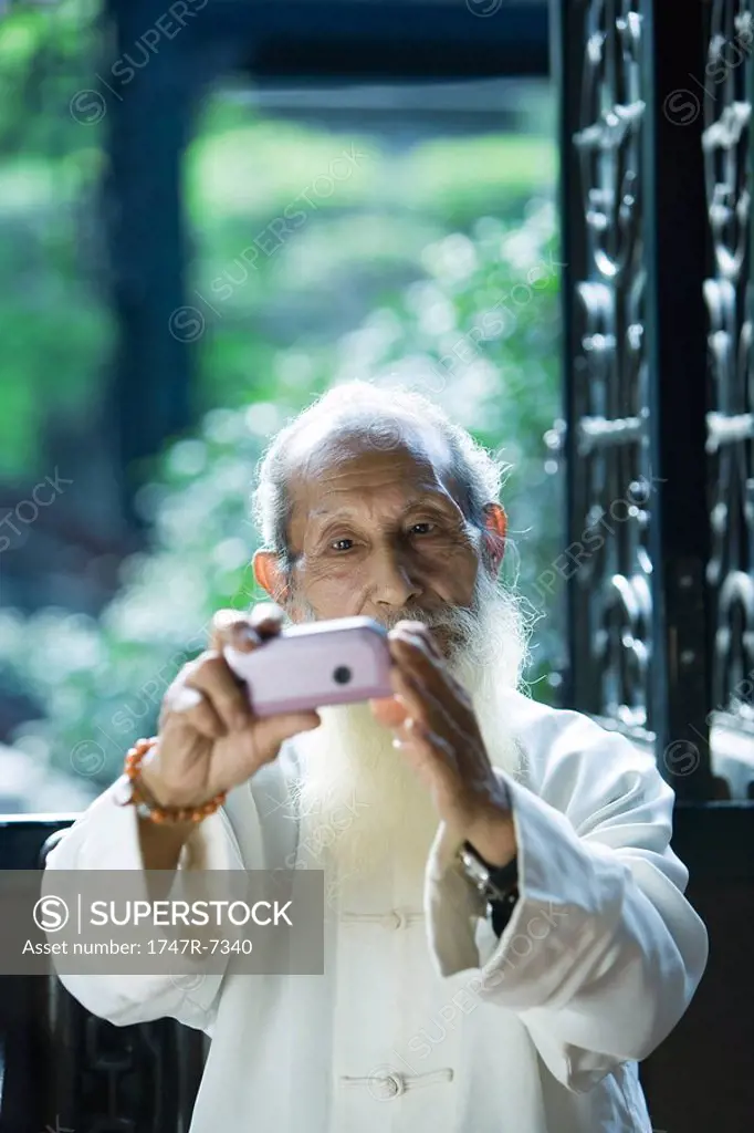 Elderly man wearing traditional Chinese clothing using camera phone