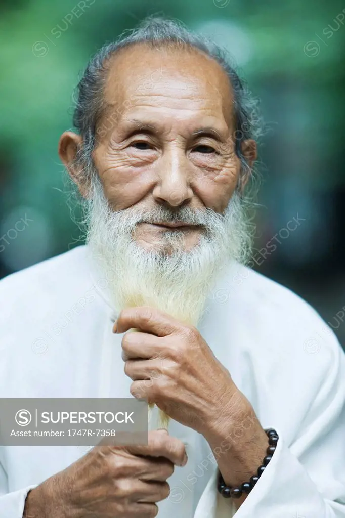 Elderly man holding long white beard in hands, portrait