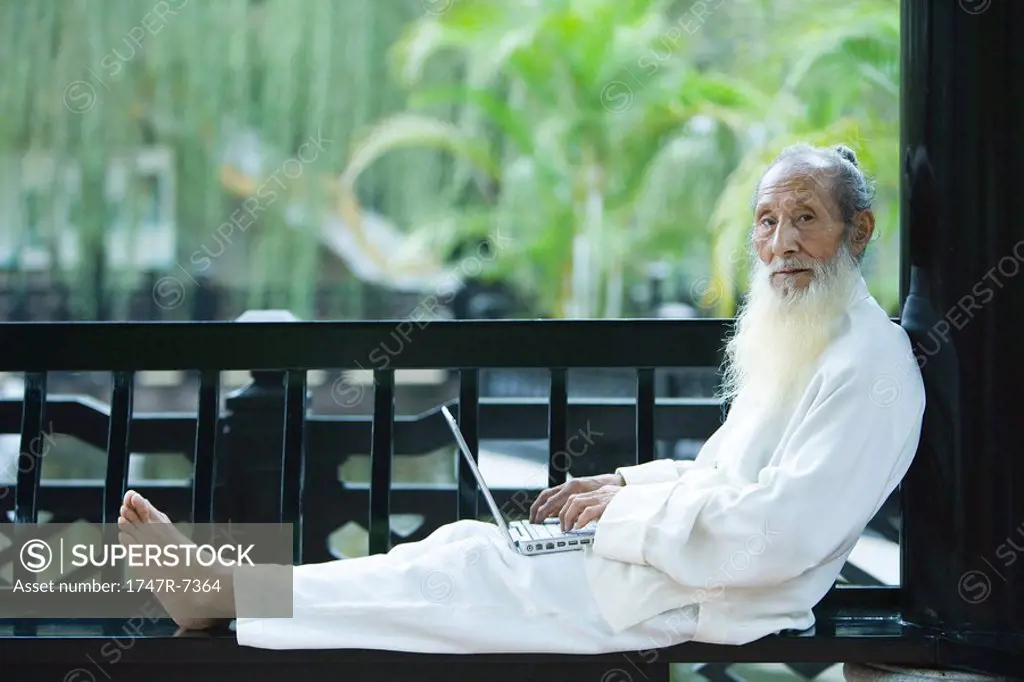 Elderly man wearing traditional Chinese clothing, using laptop, full length