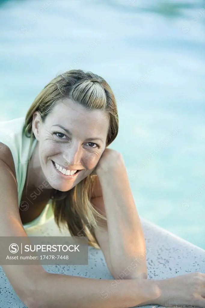 Woman lying by edge of pool, smiling at camera