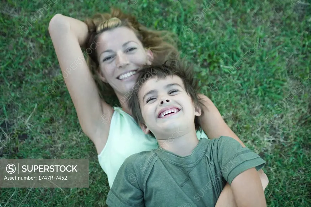 Boy and mother, boy lying on top of woman, on grass, high angle view