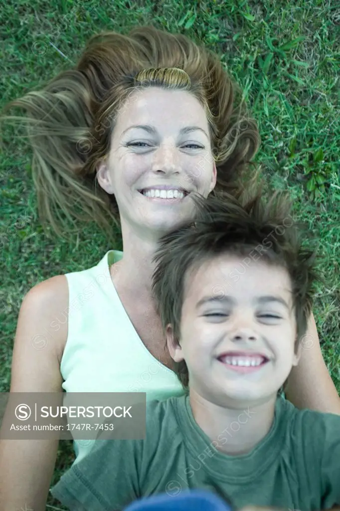 Mother and son, boy lying on top of woman, laughing, lying on grass, high angle view