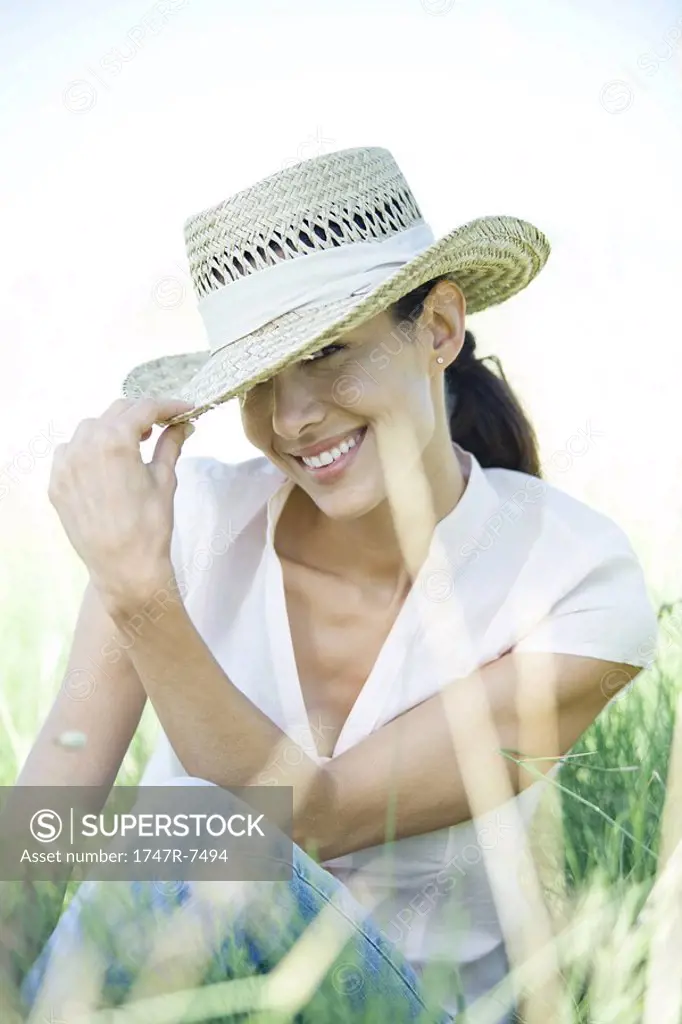 Woman in field, holding edge of hat