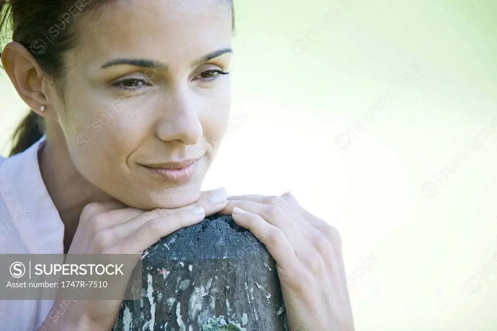 Woman leaning on wooden post, smiling, looking away, close-up