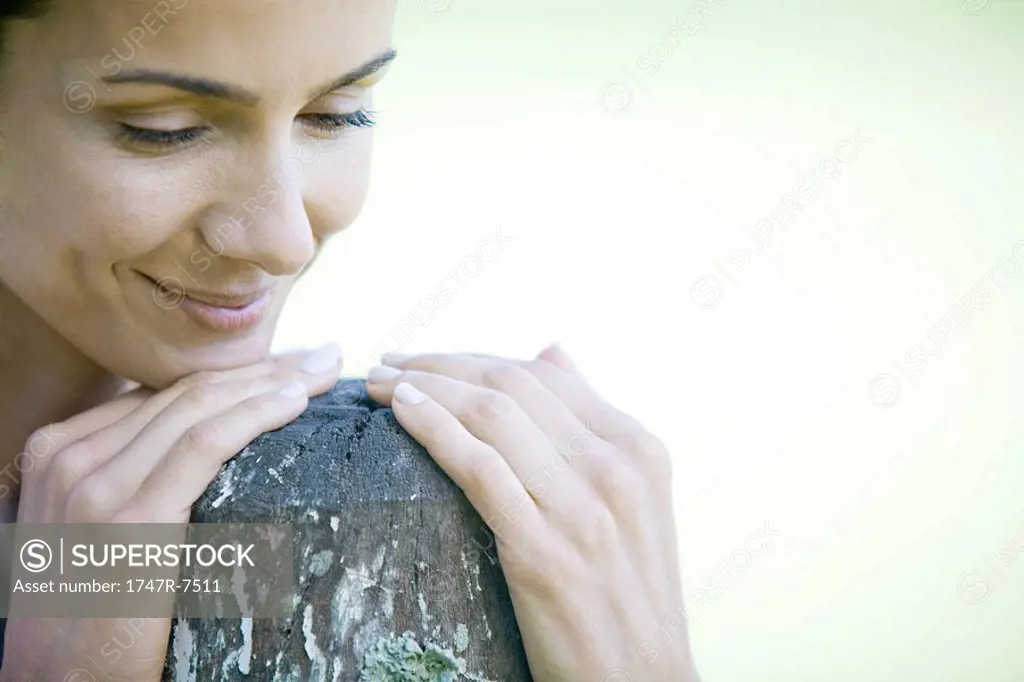 Woman leaning on wooden post, smiling, looking down, close-up