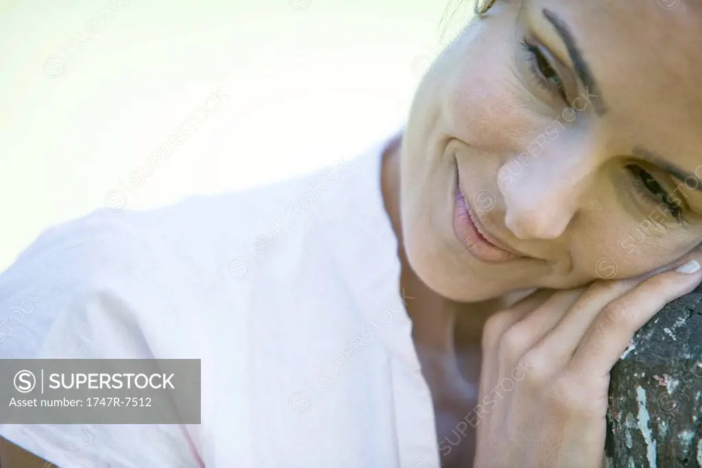 Woman leaning head on wooden post, smiling, looking away, close-up