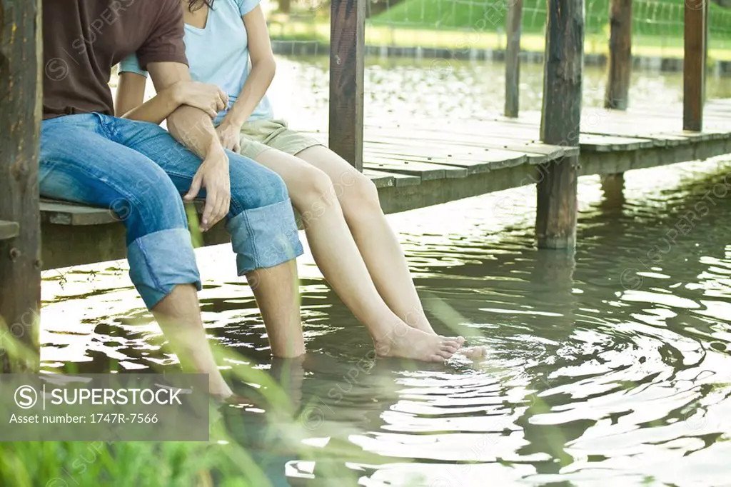 Couple sitting on dock, dangling legs in water, chest down