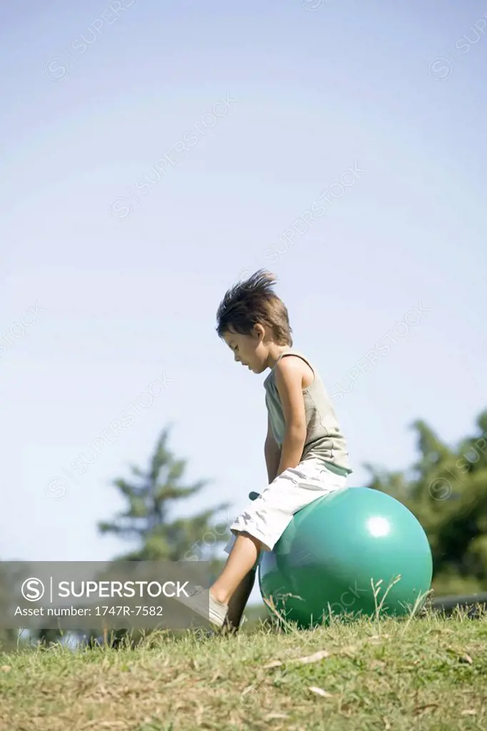 Little boy outdoors sitting on ball, full length