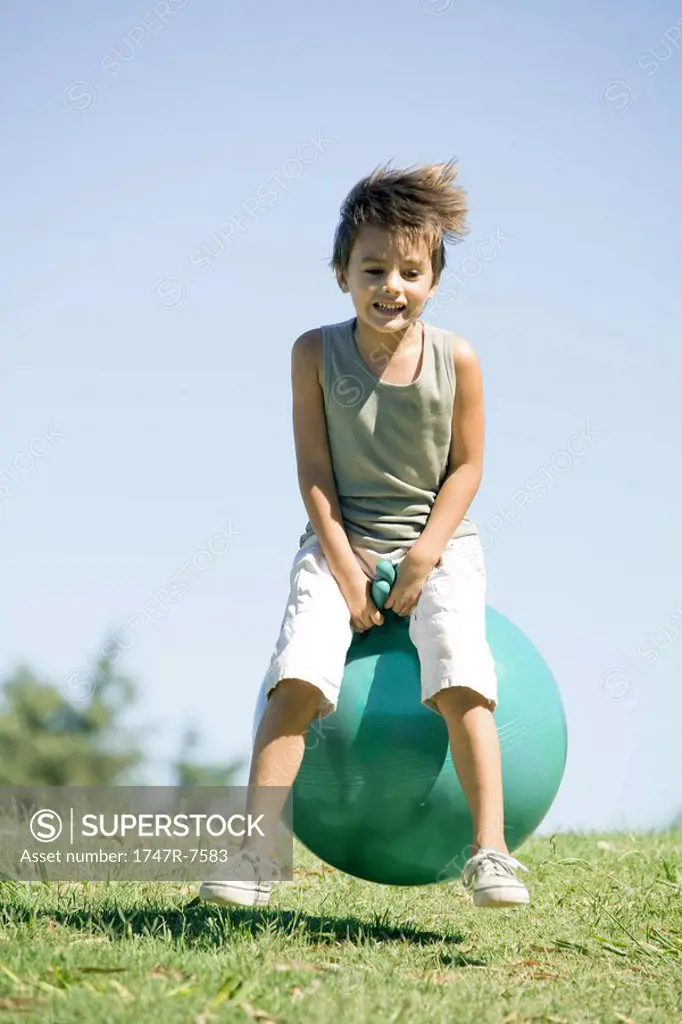 Little boy outdoors, jumping on ball, full length