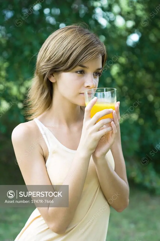 Young woman holding up glass of orange juice, looking out of frame