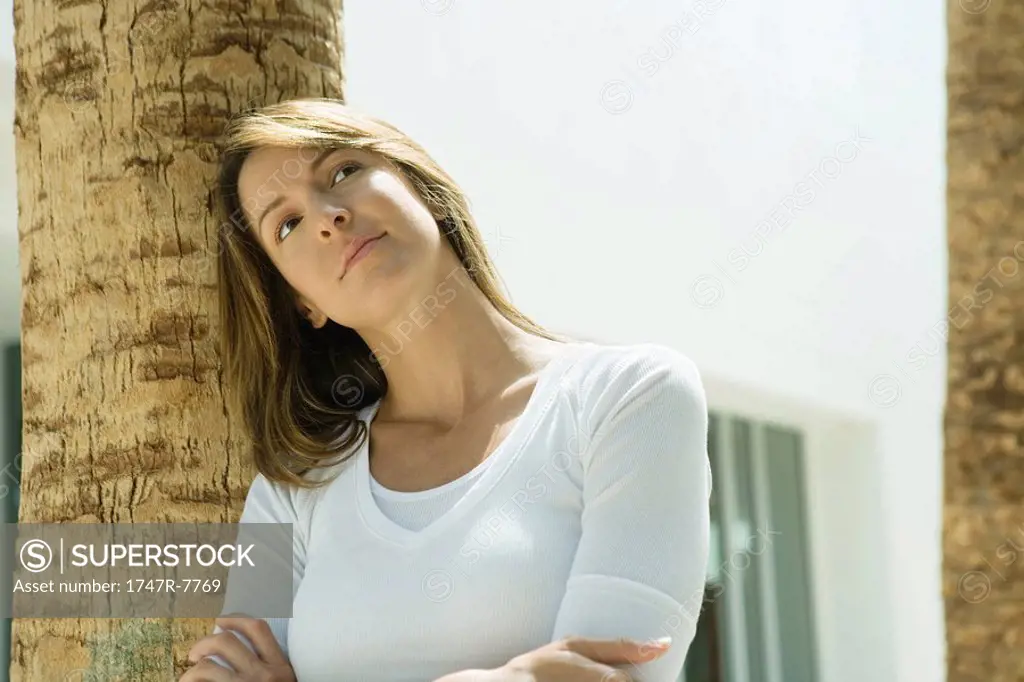 Woman with arms crossed, leaning against palm tree