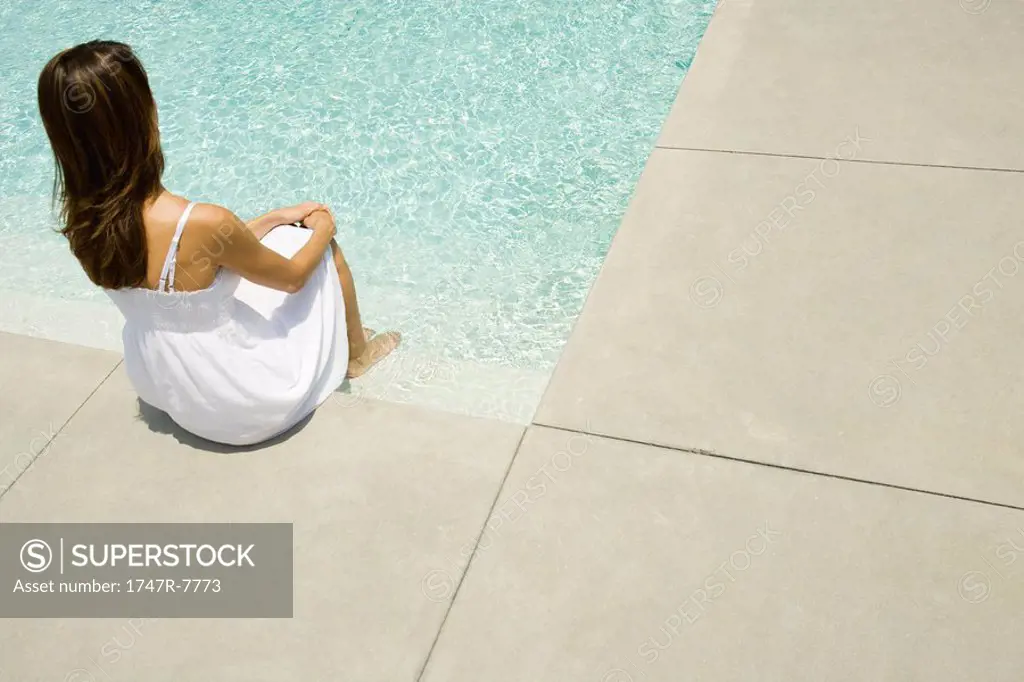 Woman sitting on edge of pool, rear view