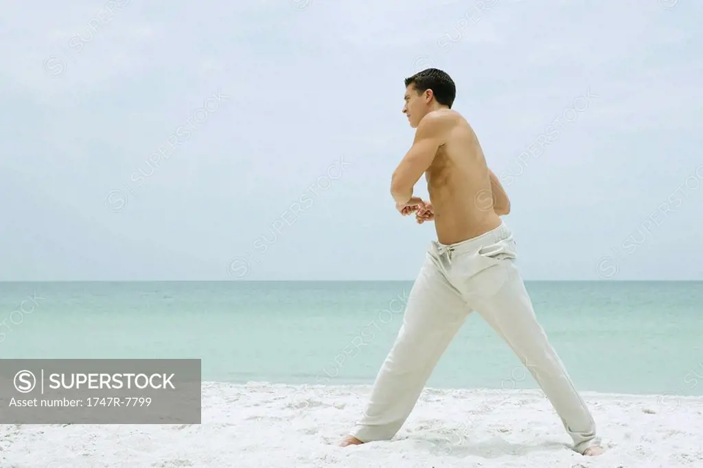 Man standing on beach, stretching, full length