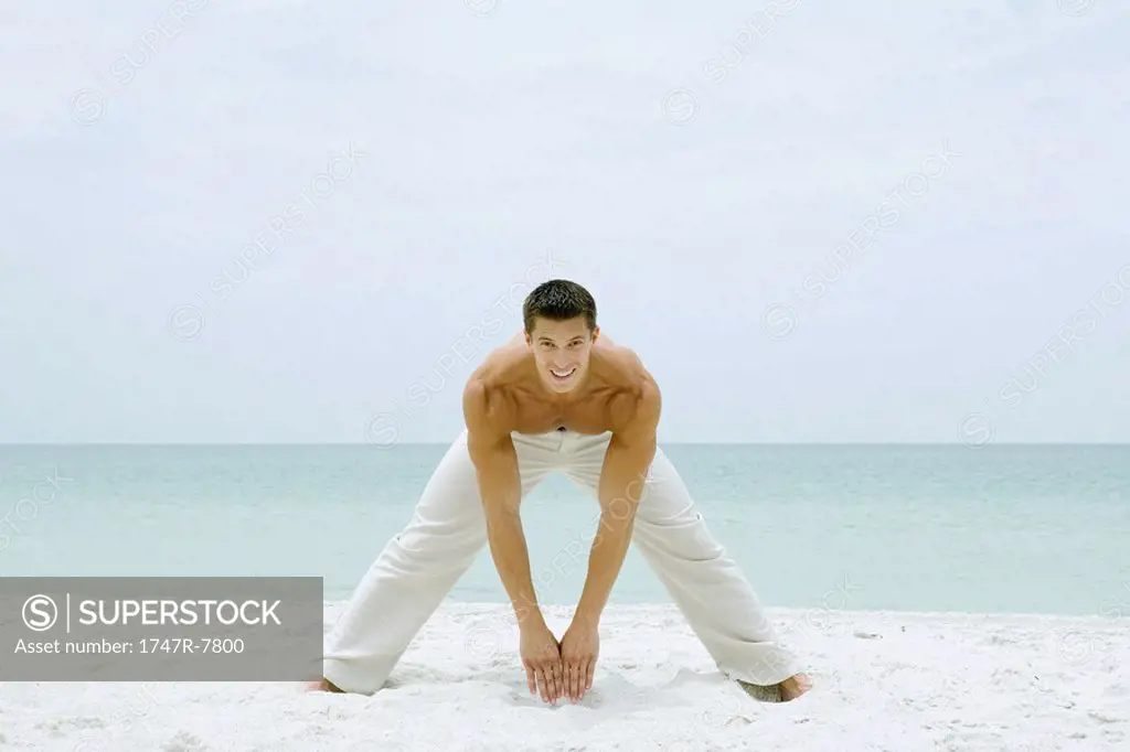 Man standing on beach, stretching and smiling at camera, full length
