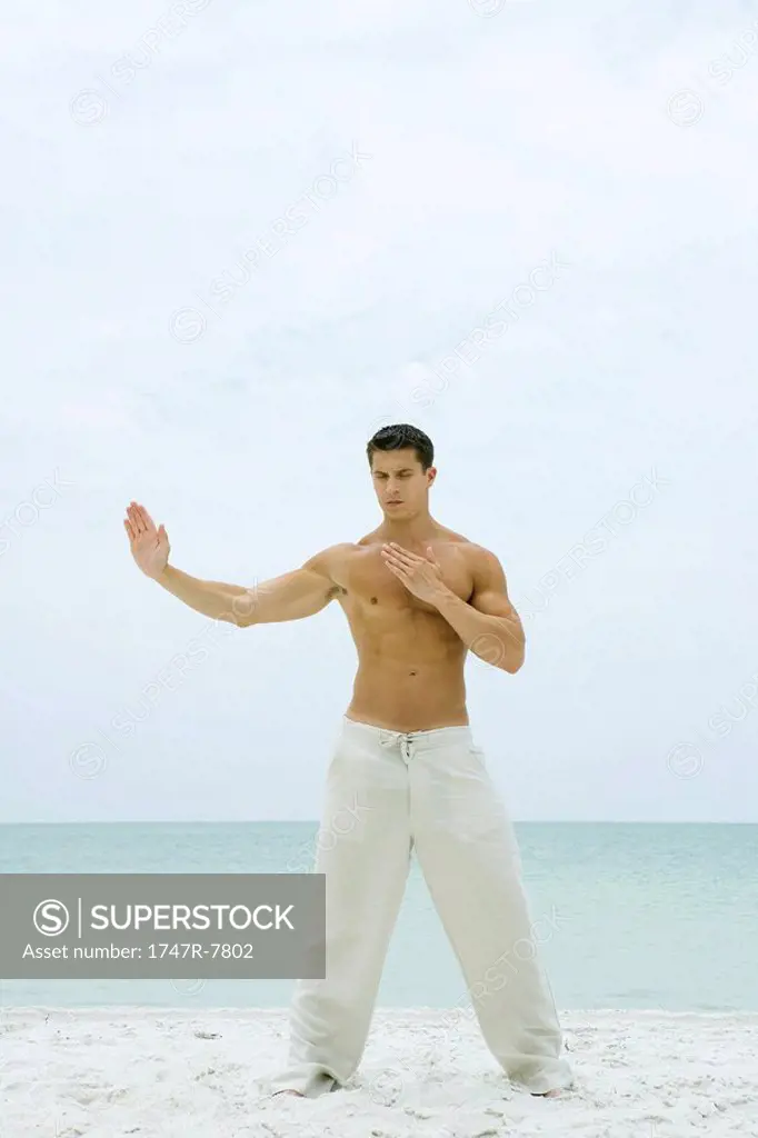 Man standing on beach, doing tai chi, full length