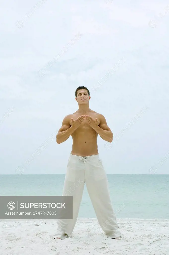 Man standing on beach, doing yoga, full length