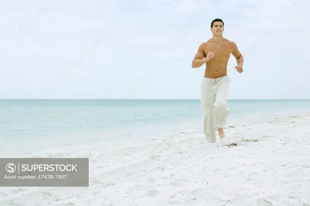 Man running on beach, smiling at camera, full length