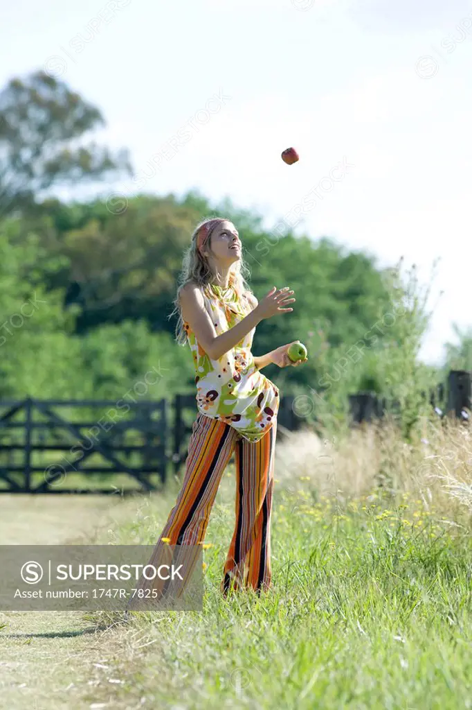 Young woman standing in field, juggling apples